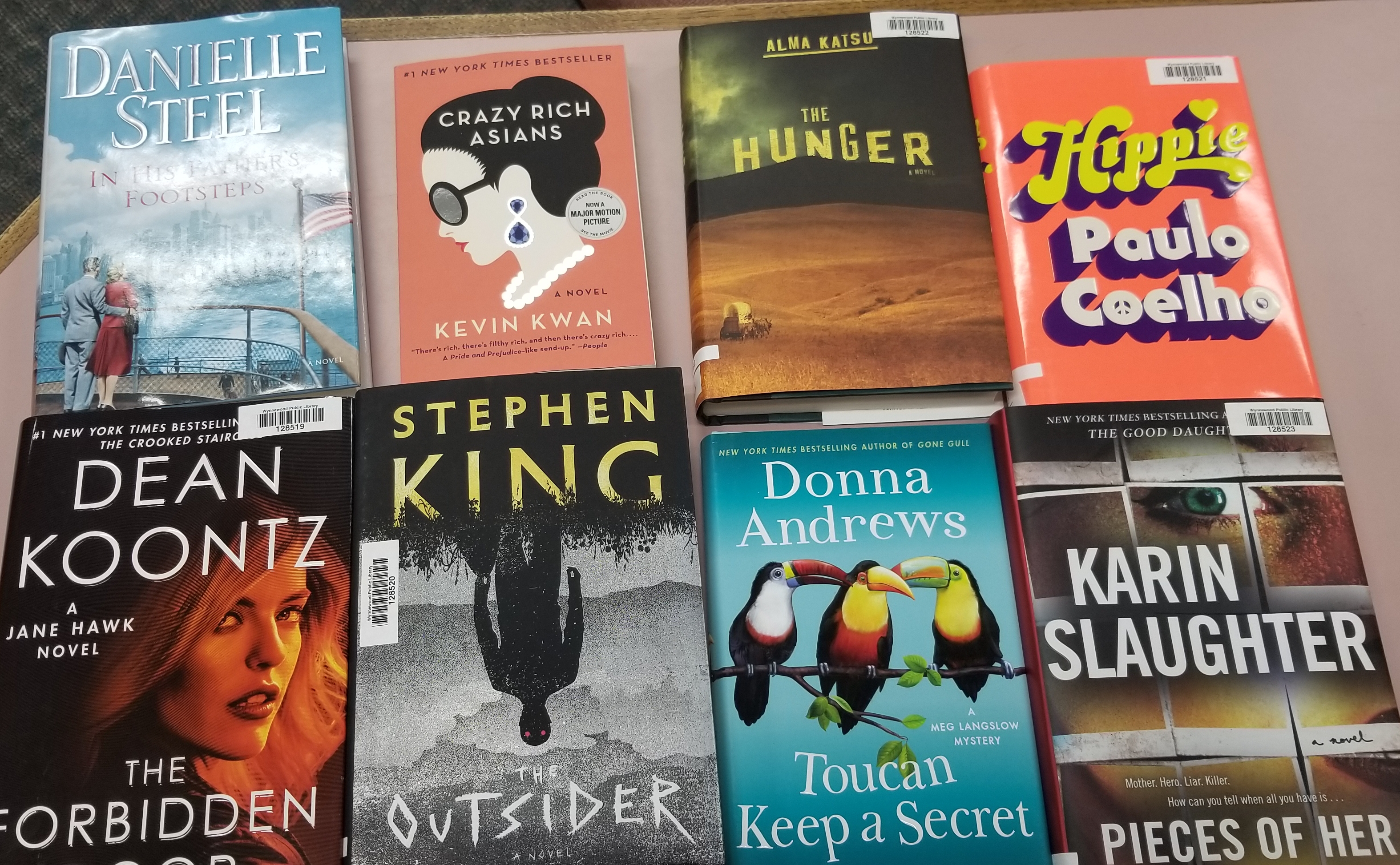 books displayed on a counter. Danielle steel, dean koontz, stephen king, the hunger, kevin kwan, donna andrews, paulo coelho