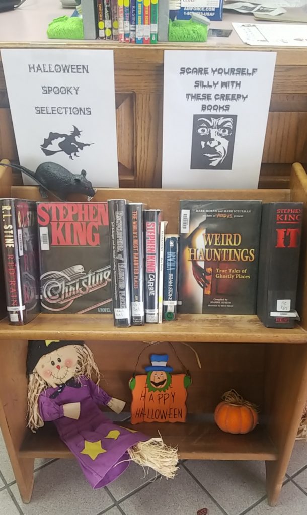 book display with halloween decorations, stephen king novels, and spooky signs along with a black rat and purple scare crow