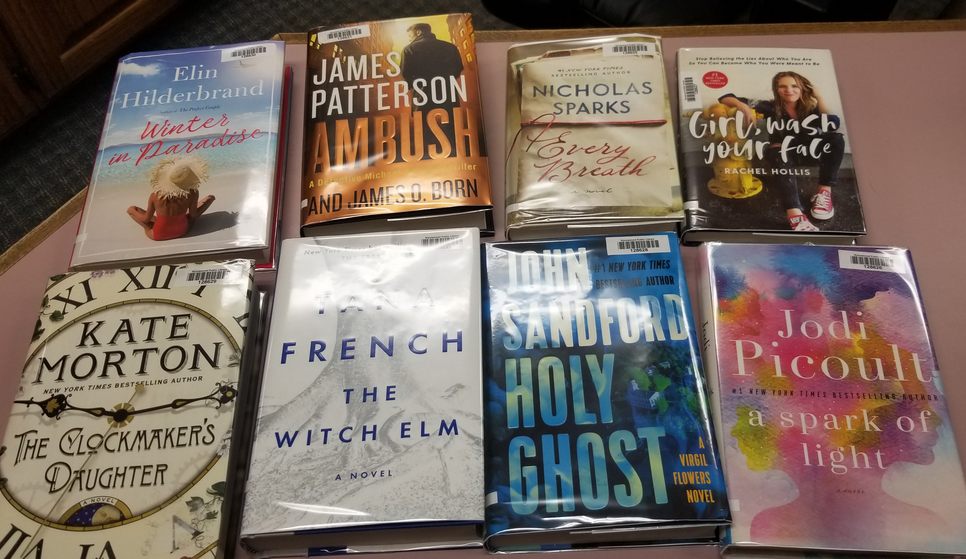 eight books on a table. Winter in paradise by Elin Hilderbrand. Ambush by James Patterson. Every Breath by Nicholas Sparks. Girl Wash Your Face by Rachel Hollis. The Clockmaker's Daughter by Kate Morton. The Witch Elm by Tana French. Holy Ghost by John Sandford. A Spark of Light by Jodi Picoult.